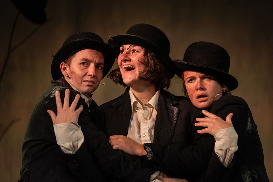 Three performers wearing bowler hats hold each other, making different ...